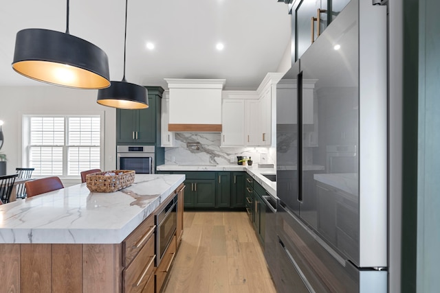 kitchen with a kitchen island, stainless steel appliances, pendant lighting, white cabinets, and light hardwood / wood-style flooring