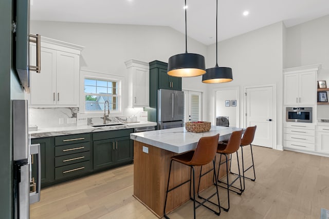 kitchen featuring a kitchen island, sink, white cabinets, pendant lighting, and appliances with stainless steel finishes