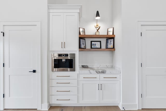 bar featuring light stone countertops, light wood-type flooring, white cabinets, and oven