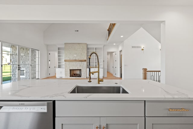 kitchen with a stone fireplace, sink, vaulted ceiling, stainless steel dishwasher, and light stone counters