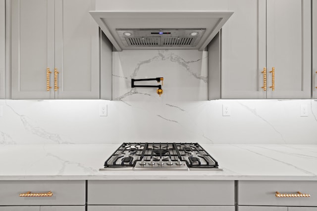 kitchen with extractor fan, stainless steel gas stovetop, light stone counters, and gray cabinetry