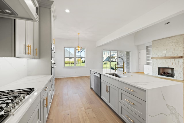 kitchen with gray cabinetry, stainless steel appliances, sink, decorative light fixtures, and light wood-type flooring