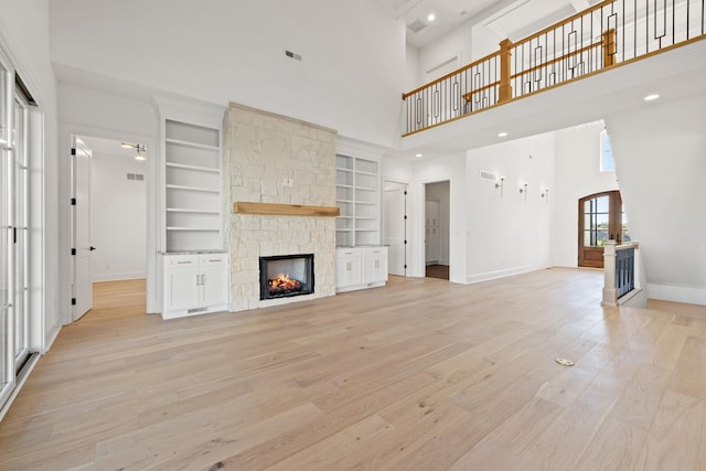 unfurnished living room featuring a high ceiling, light hardwood / wood-style flooring, a fireplace, and built in features