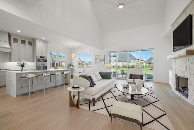 living room with light hardwood / wood-style flooring, high vaulted ceiling, a fireplace, and plenty of natural light