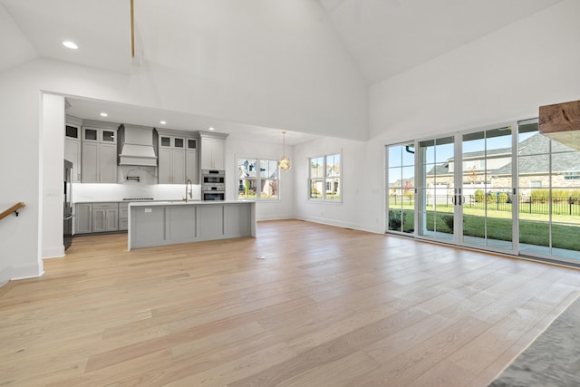 kitchen with sink, light hardwood / wood-style floors, pendant lighting, custom exhaust hood, and a center island with sink