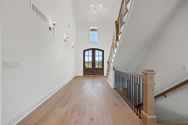 entrance foyer featuring a towering ceiling, french doors, an inviting chandelier, and light hardwood / wood-style floors