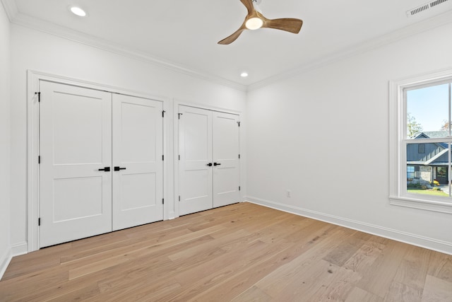 unfurnished bedroom with ceiling fan, ornamental molding, light hardwood / wood-style flooring, and two closets