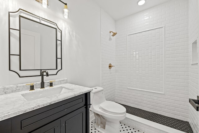 bathroom with toilet, vanity, a tile shower, and tile patterned flooring