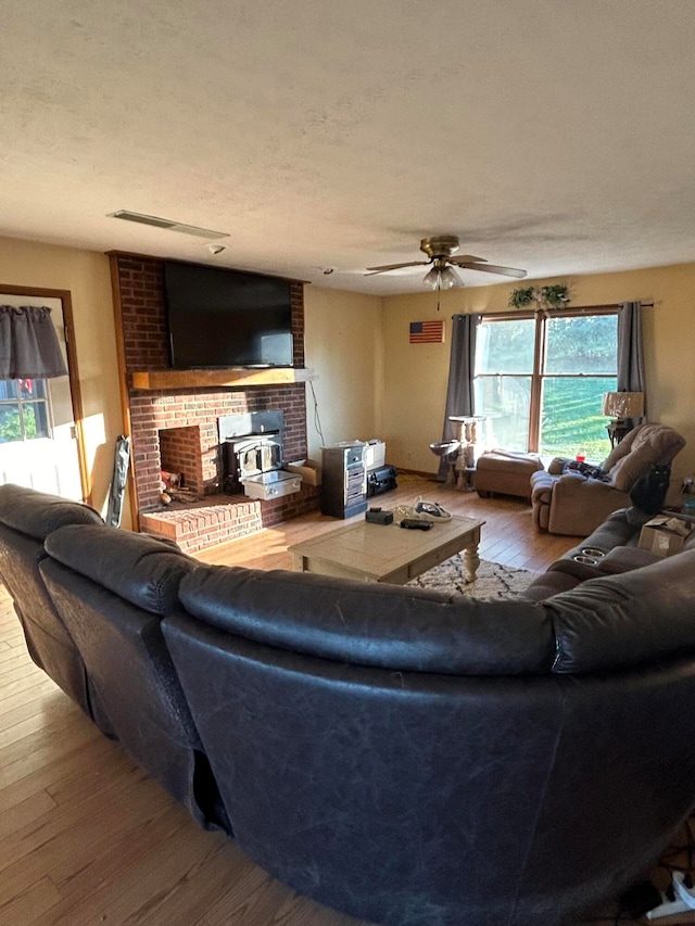 living room with hardwood / wood-style floors, ceiling fan, a wood stove, and plenty of natural light