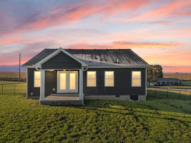 back house at dusk with a lawn, a patio, and french doors