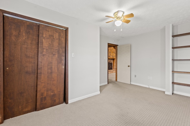 unfurnished bedroom with ceiling fan, a textured ceiling, a stone fireplace, a closet, and light colored carpet