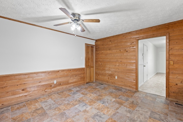 empty room featuring ceiling fan, a textured ceiling, and wooden walls