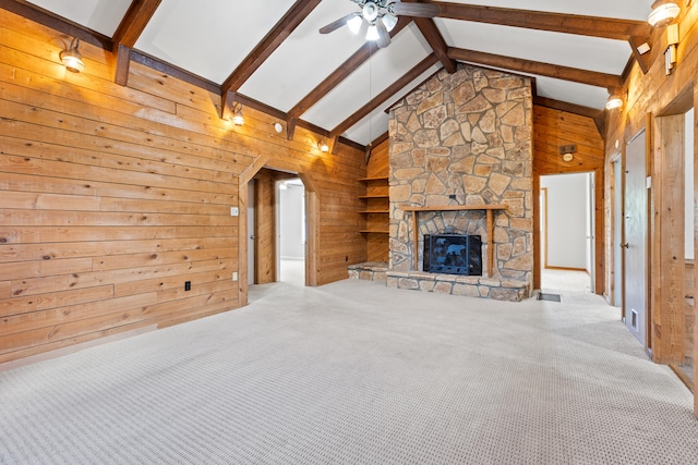 unfurnished living room featuring a stone fireplace, wood walls, beam ceiling, and carpet