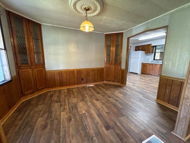 unfurnished dining area with a healthy amount of sunlight, a textured ceiling, dark hardwood / wood-style floors, and wood walls