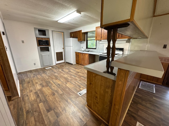 kitchen with kitchen peninsula, a breakfast bar area, dark wood-type flooring, sink, and white appliances