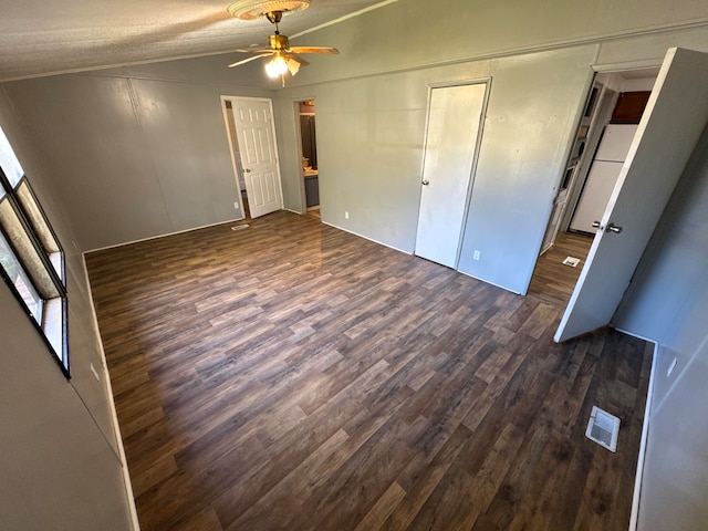 unfurnished bedroom with ceiling fan, a textured ceiling, vaulted ceiling, dark hardwood / wood-style floors, and white fridge