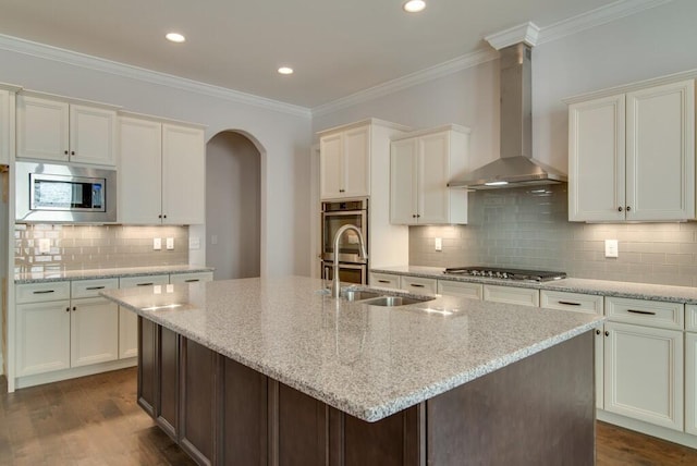 kitchen with wall chimney range hood, stainless steel appliances, and an island with sink