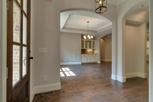 foyer entrance with a notable chandelier, crown molding, a tray ceiling, and dark hardwood / wood-style flooring