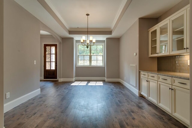 unfurnished dining area with an inviting chandelier, crown molding, dark hardwood / wood-style floors, and a tray ceiling