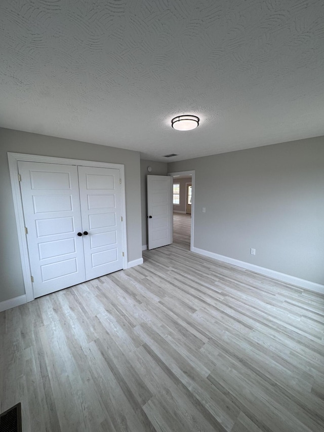 unfurnished bedroom featuring light wood-type flooring, a closet, and a textured ceiling