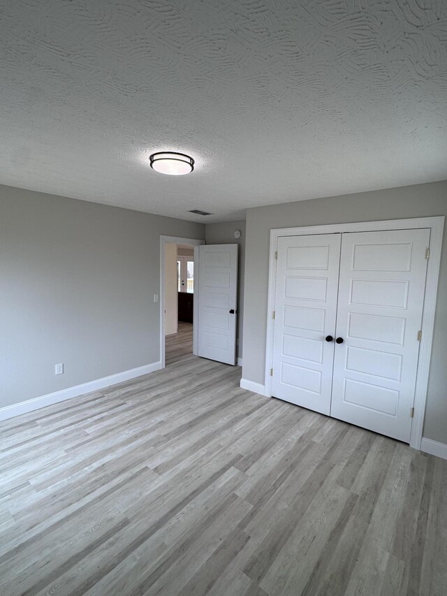 unfurnished bedroom featuring a textured ceiling, light hardwood / wood-style floors, and a closet