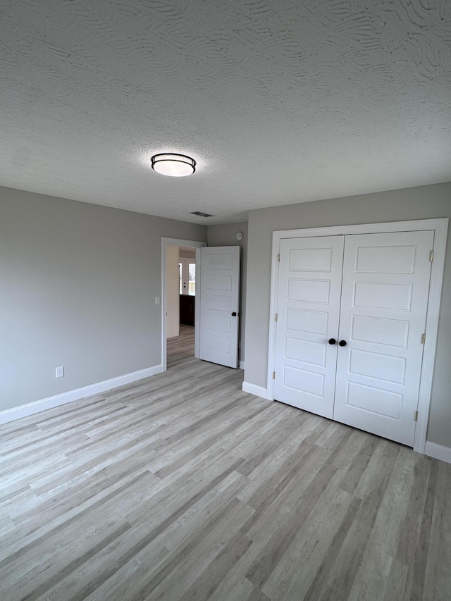 unfurnished bedroom with light wood-type flooring, a textured ceiling, and a closet