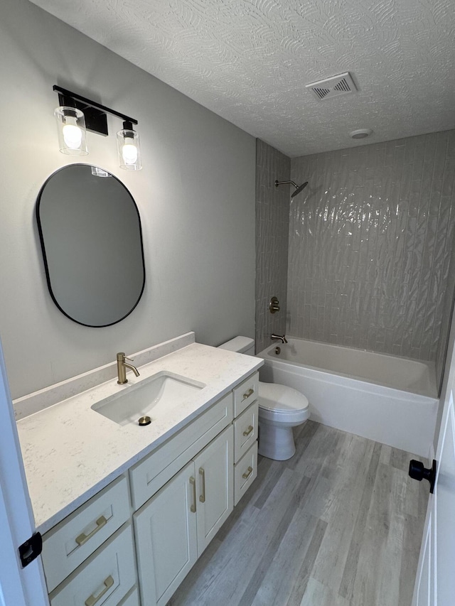 full bathroom with tiled shower / bath combo, toilet, wood-type flooring, a textured ceiling, and vanity