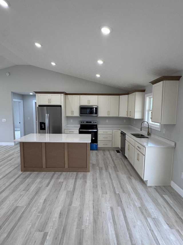 kitchen with appliances with stainless steel finishes, sink, vaulted ceiling, light hardwood / wood-style flooring, and a kitchen island