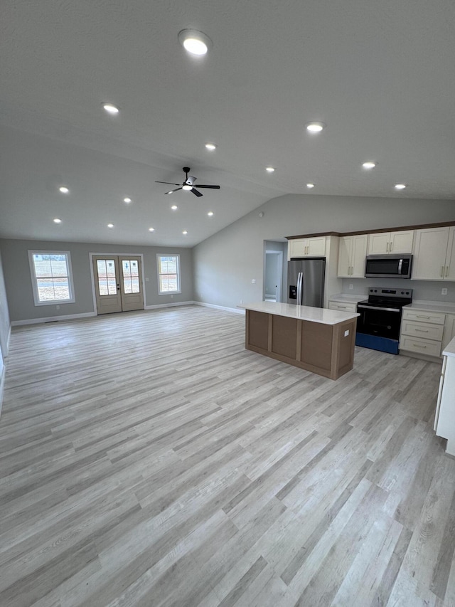 kitchen with appliances with stainless steel finishes, lofted ceiling, a center island, white cabinetry, and light hardwood / wood-style floors