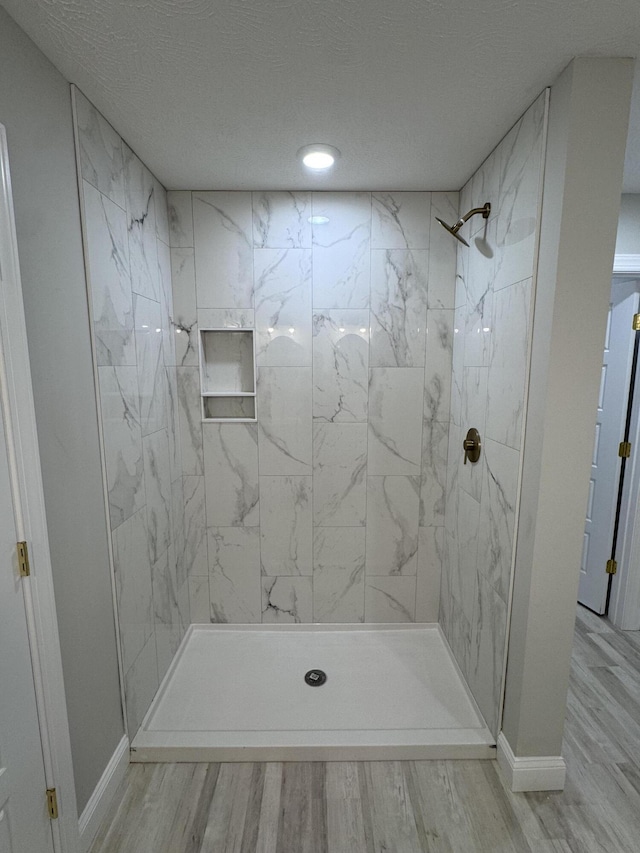 bathroom with wood-type flooring, a textured ceiling, and a tile shower