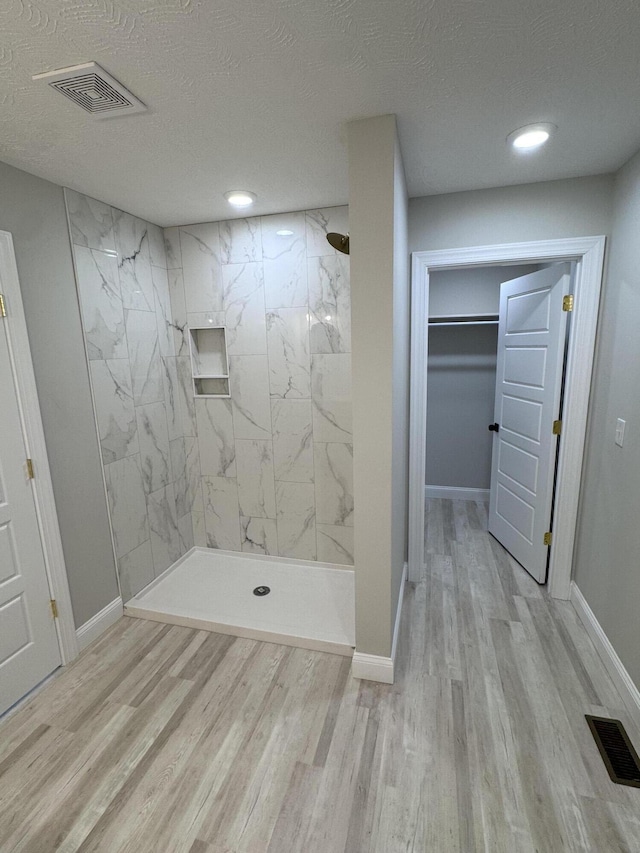 bathroom featuring a tile shower, wood-type flooring, and a textured ceiling