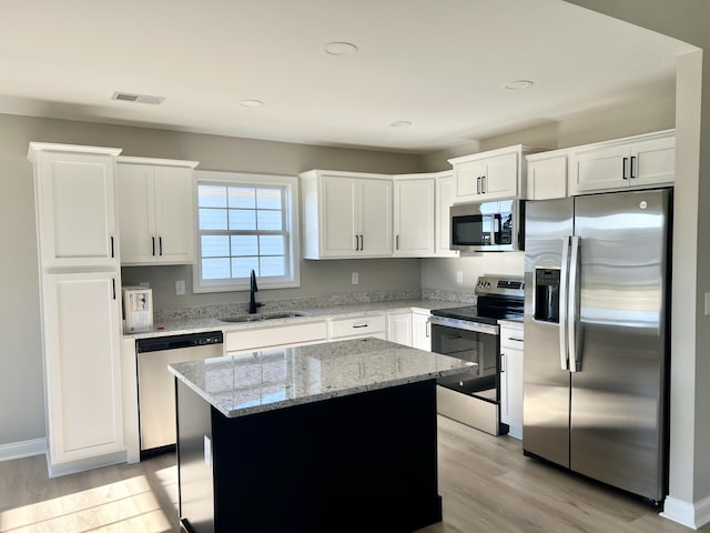 kitchen featuring a kitchen island, light stone counters, light wood-style flooring, stainless steel appliances, and a sink