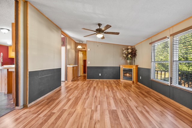 unfurnished living room featuring light wood-type flooring, a textured ceiling, ceiling fan, vaulted ceiling, and crown molding