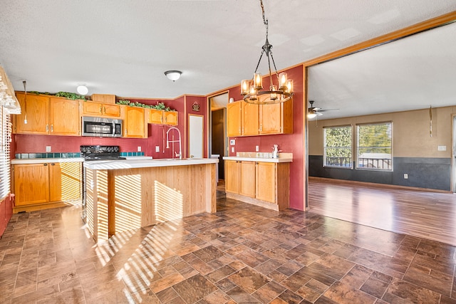 kitchen featuring a kitchen island with sink, black stove, dark wood-type flooring, hanging light fixtures, and ceiling fan with notable chandelier