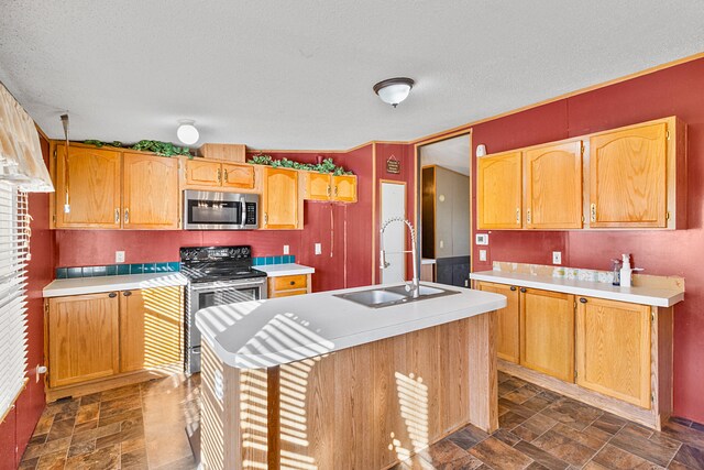 kitchen with an island with sink, a textured ceiling, sink, and stainless steel appliances