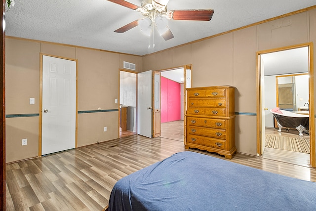 bedroom featuring ceiling fan, a textured ceiling, light hardwood / wood-style flooring, ornamental molding, and ensuite bath