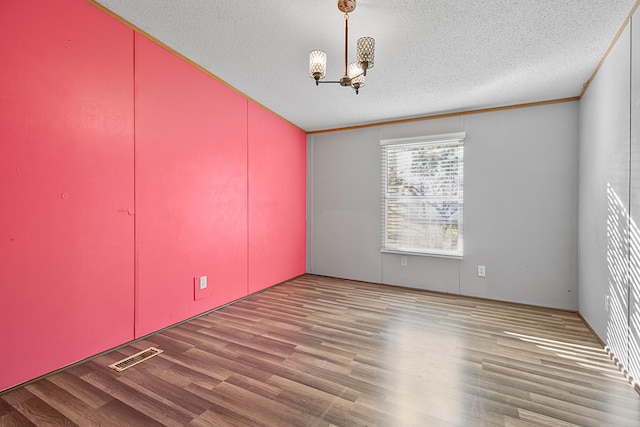 empty room with hardwood / wood-style flooring, a textured ceiling, an inviting chandelier, and ornamental molding