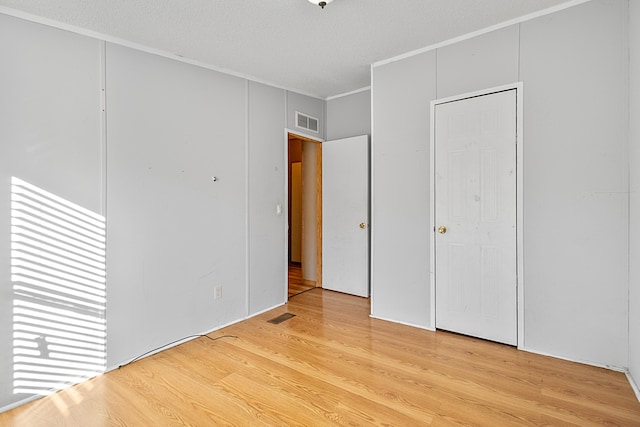 unfurnished bedroom featuring light hardwood / wood-style floors, a textured ceiling, and ornamental molding