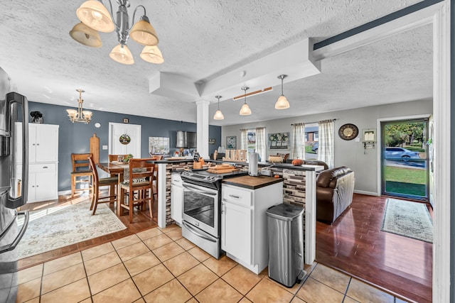 kitchen featuring stainless steel stove, pendant lighting, white cabinets, a textured ceiling, and light hardwood / wood-style floors