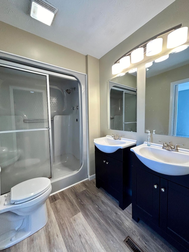 bathroom with a textured ceiling, hardwood / wood-style floors, toilet, walk in shower, and vanity