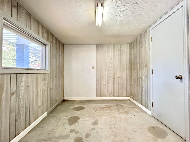 unfurnished room with a textured ceiling, wooden walls, and concrete flooring