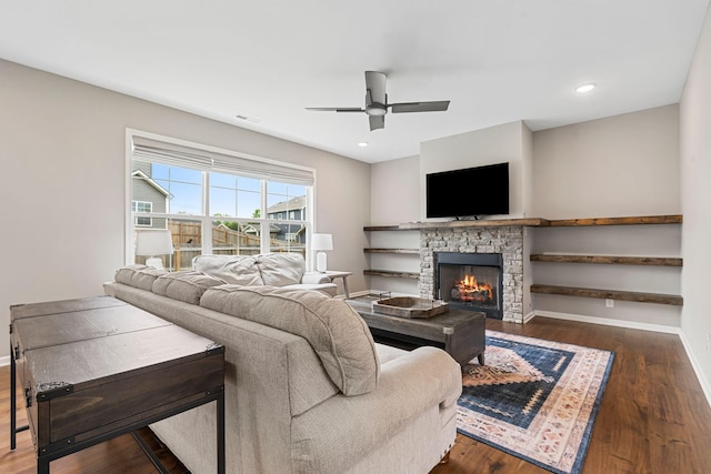 living room featuring a stone fireplace, dark hardwood / wood-style floors, and ceiling fan