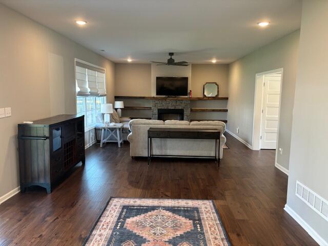 living room featuring a stone fireplace, ceiling fan, and dark hardwood / wood-style flooring