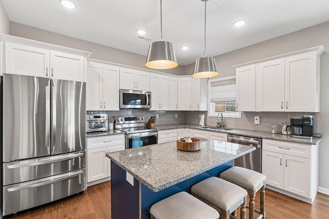 kitchen featuring white cabinets, hanging light fixtures, stainless steel appliances, sink, and a center island