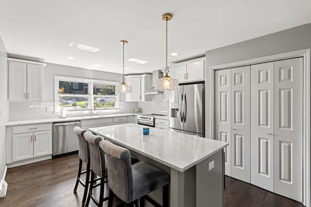 kitchen with a kitchen island, dark hardwood / wood-style flooring, stainless steel appliances, pendant lighting, and white cabinets