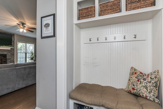 mudroom with a stone fireplace, wood-type flooring, and ceiling fan