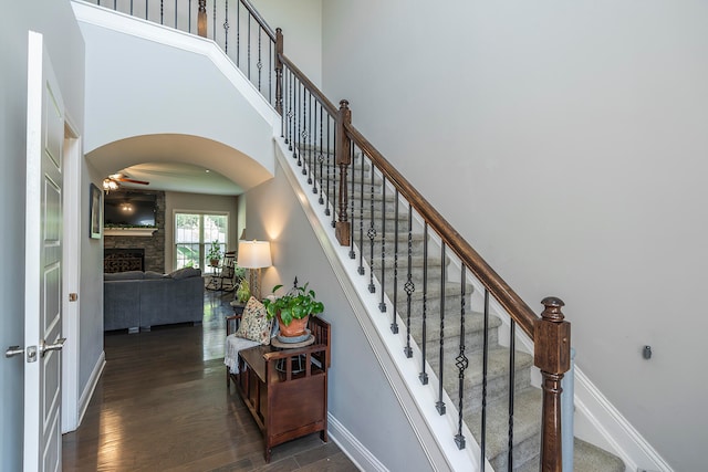 staircase featuring a stone fireplace, hardwood / wood-style flooring, and a towering ceiling