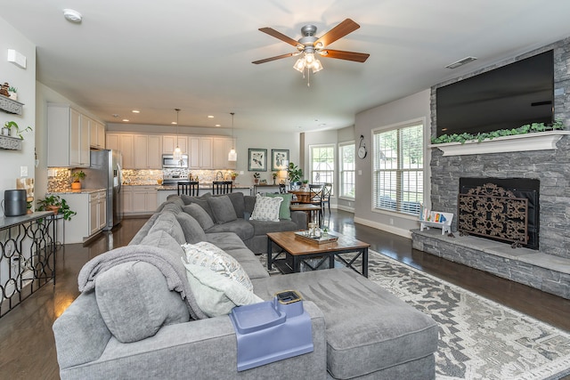 living room featuring a stone fireplace, dark hardwood / wood-style floors, and ceiling fan