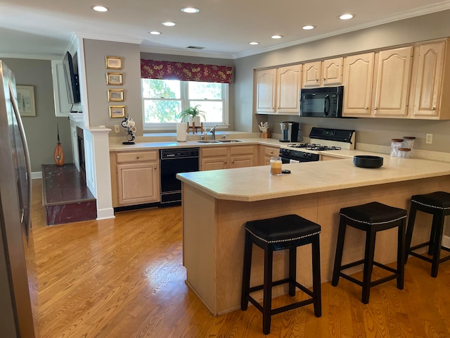 kitchen with a kitchen bar, kitchen peninsula, light wood-type flooring, crown molding, and black appliances