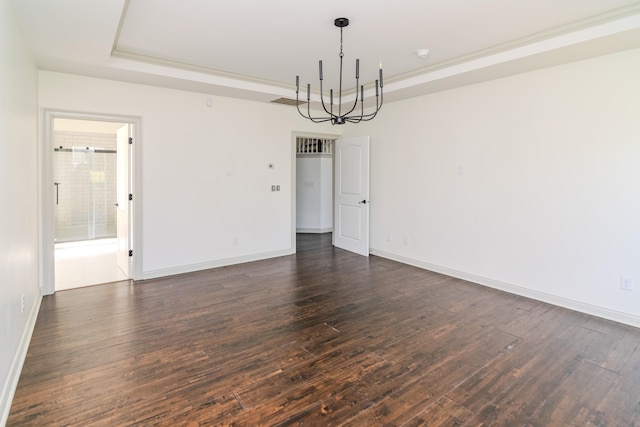 spare room with an inviting chandelier, a tray ceiling, and dark wood-type flooring